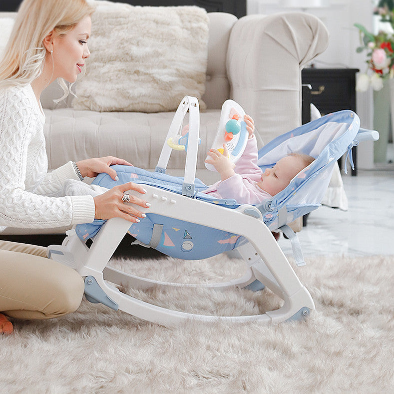 Woman sitting on the floor with a baby in a blue and white baby rocker in a living room.